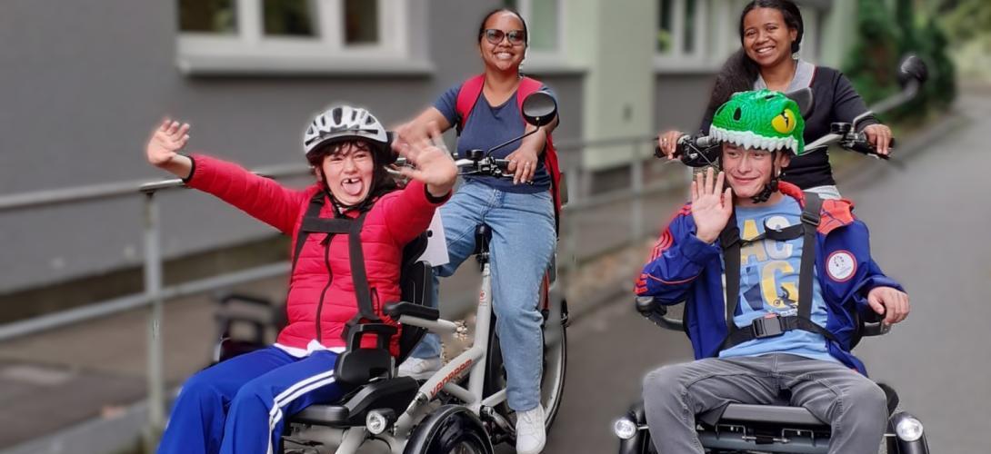 Foto von zwei Teilnehmenden der Ferienbetreuung, die mit zwei Mitarbeitenden mit dem Rollfiets unterwegs sind