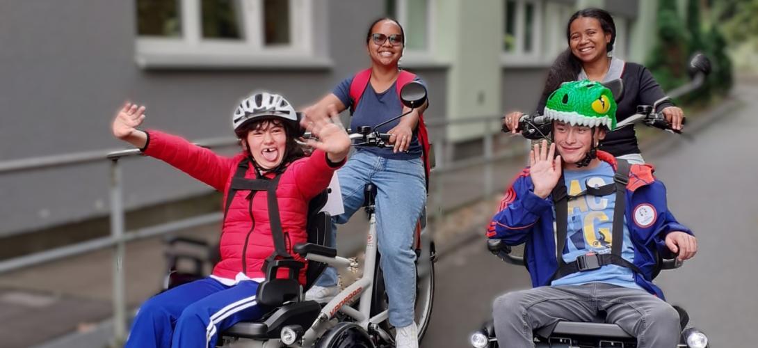 Foto von zwei Teilnehmenden der Ferienbetreuung, die mit zwei Mitarbeitenden mit dem Rollfiets unterwegs sind