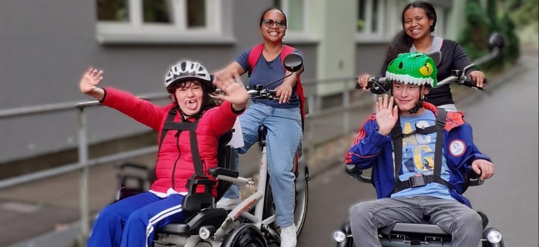 Foto von zwei Teilnehmenden der Ferienbetreuung, die mit zwei Mitarbeitenden mit dem Rollfiets unterwegs sind
