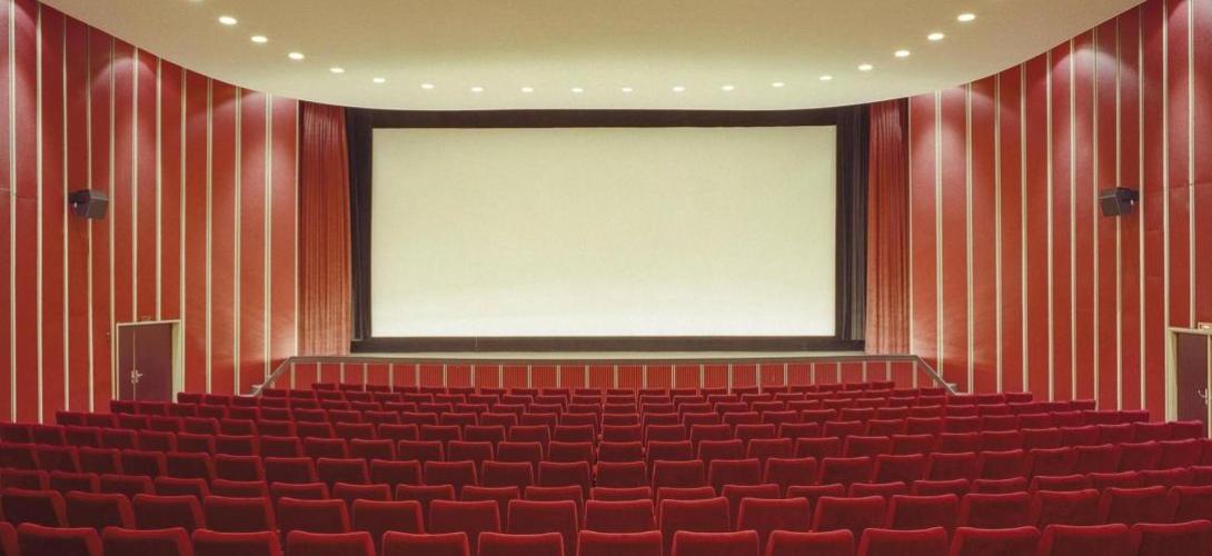 Zu sehen ist ein Kinosaal mit roten Sesseln und einer Leinwand