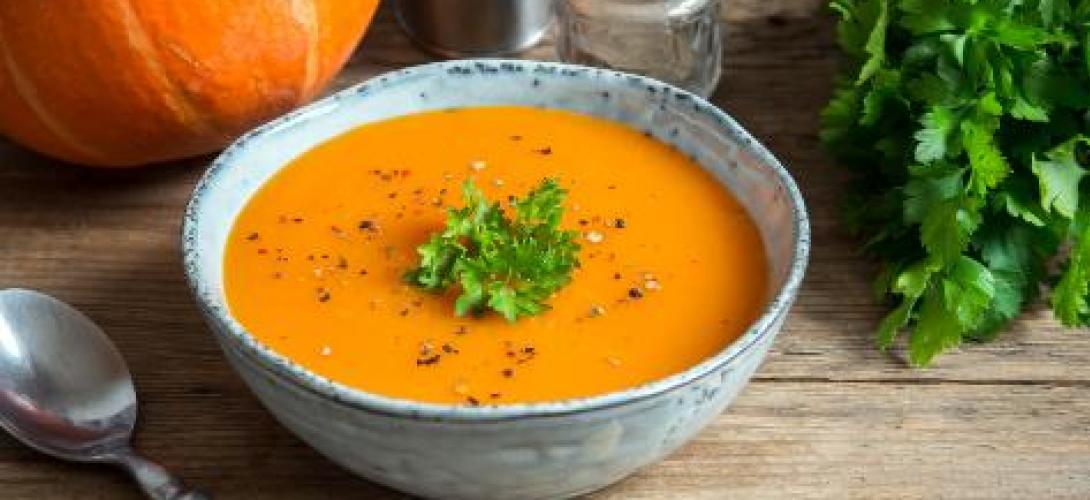Eine Schale mit Kürbissuppe, ein Löffel, etwas Petersilie und ein Teil eines Kürbisses sind zu sehen